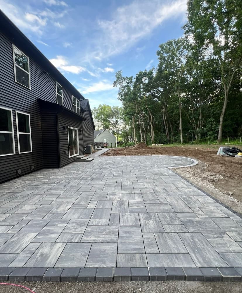 Newly paved patio with gray pavers, surrounded by greenery and modern house exterior.
