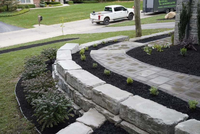 Landscaped garden with stone wall, pathway, and truck parked in background.