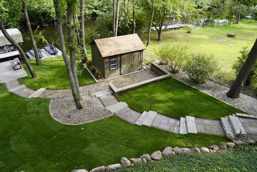 Scenic backyard with a shed, stone pathways, and lush greenery by a peaceful river.