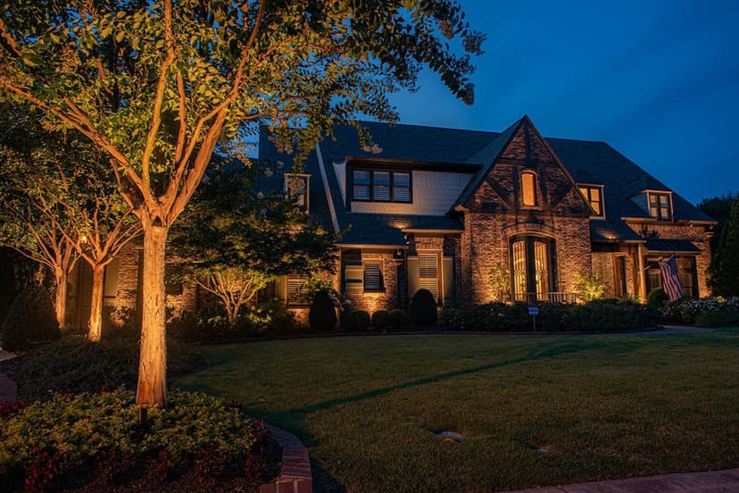 Elegant brick home illuminated at dusk with landscaped yard and mature trees.