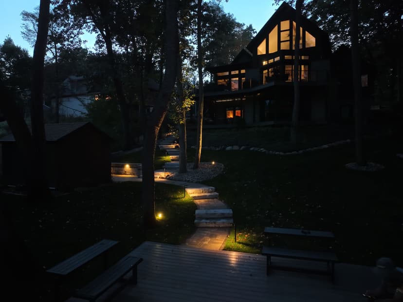 Cozy lakeside home at dusk with pathway lights illuminating a serene outdoor setting.