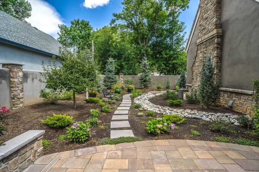 Lush backyard garden with stone path, trees, and vibrant flowers under a blue sky.