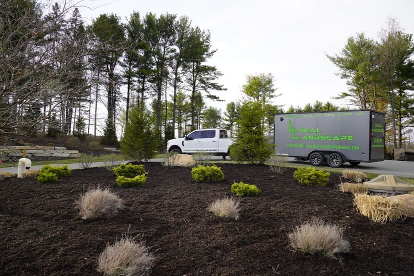 White truck and trailer labeled "Local Landscape" parked near landscaped garden with bushes.