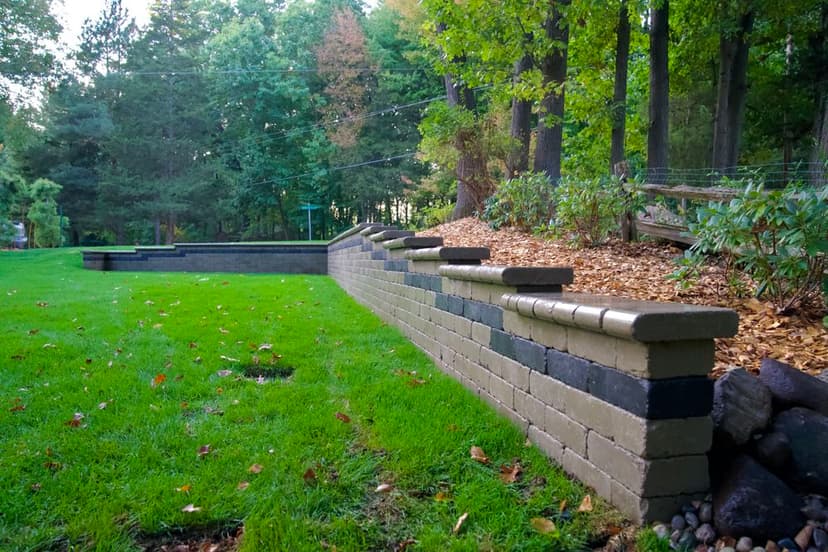 Decorative stone retaining wall in a lush green backyard with trees and fallen leaves.