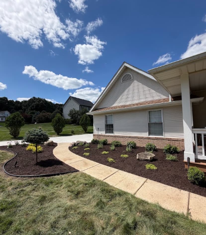 Well-landscaped home exterior with flower beds, pathways, and a clear blue sky.
