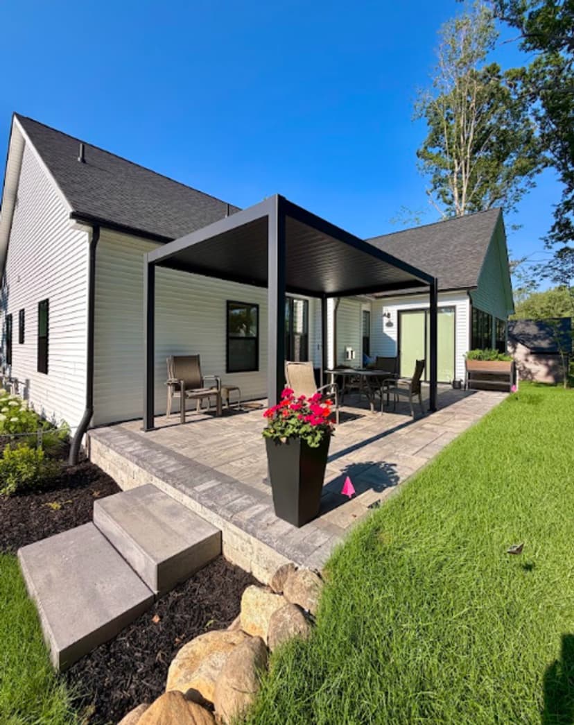 Modern patio with a black pergola, outdoor furniture, and vibrant flower planter.