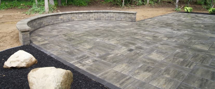 Patio installation featuring stone pavers and a curved seating wall in a natural setting.